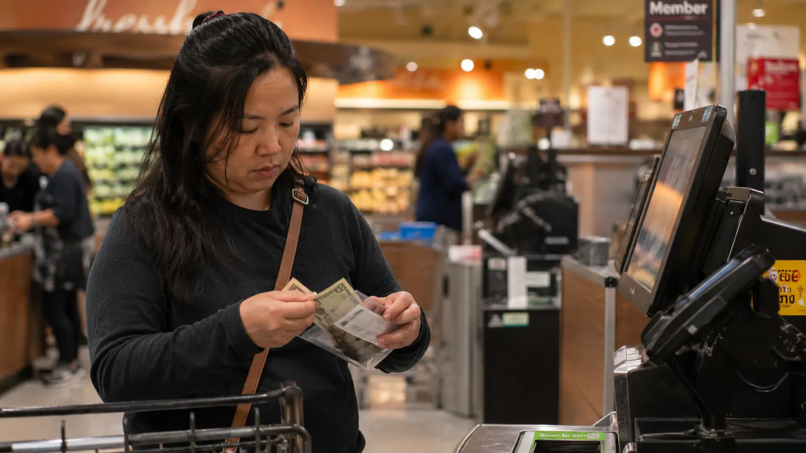 Person at a grocery store checkout handing over cash from a labeled budget envelope